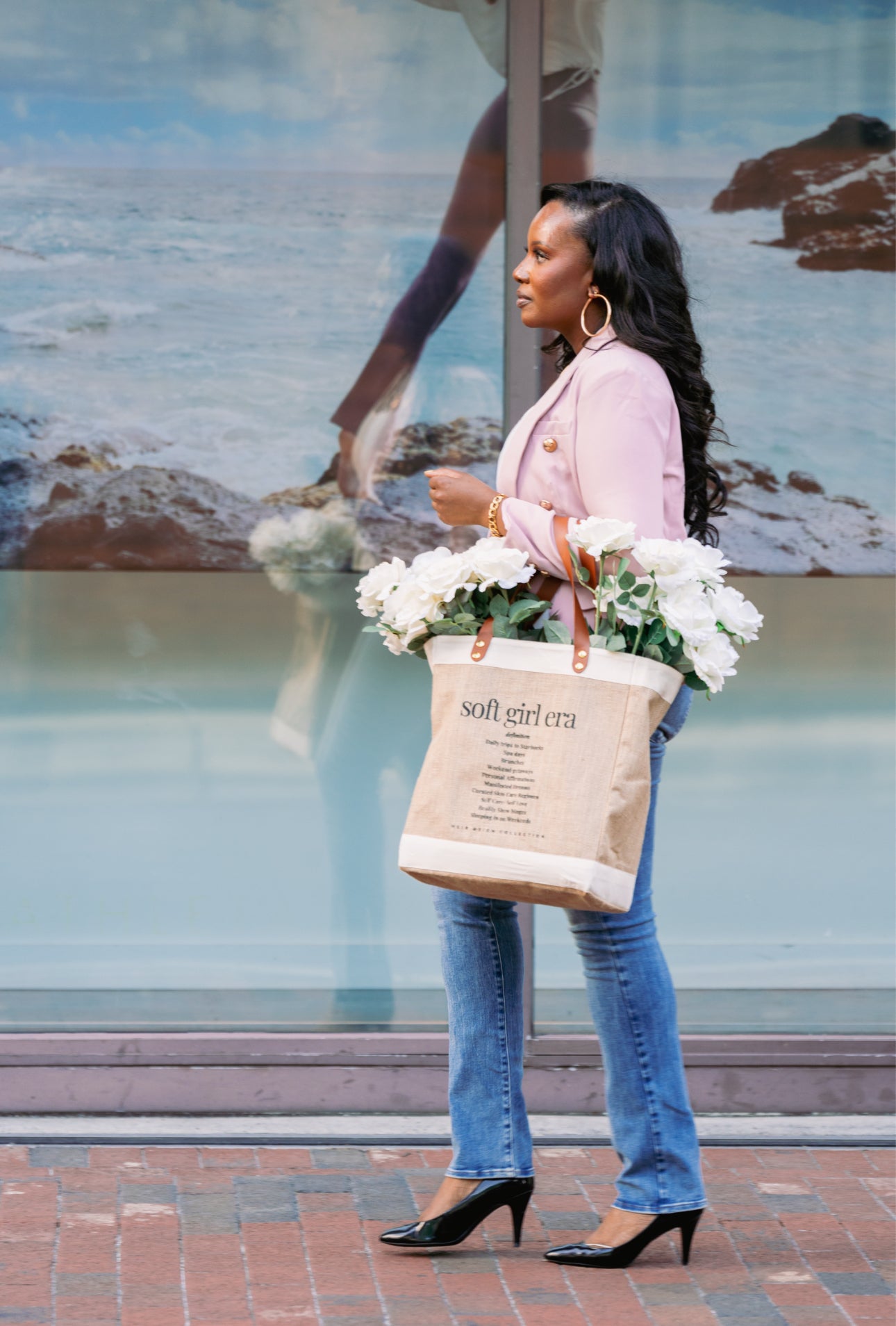 This is a picture of a burlap tote bag with a positive affirmation quote on the front. There is a woman holding the tote bag that has bright white summer flowers inside of the bag.