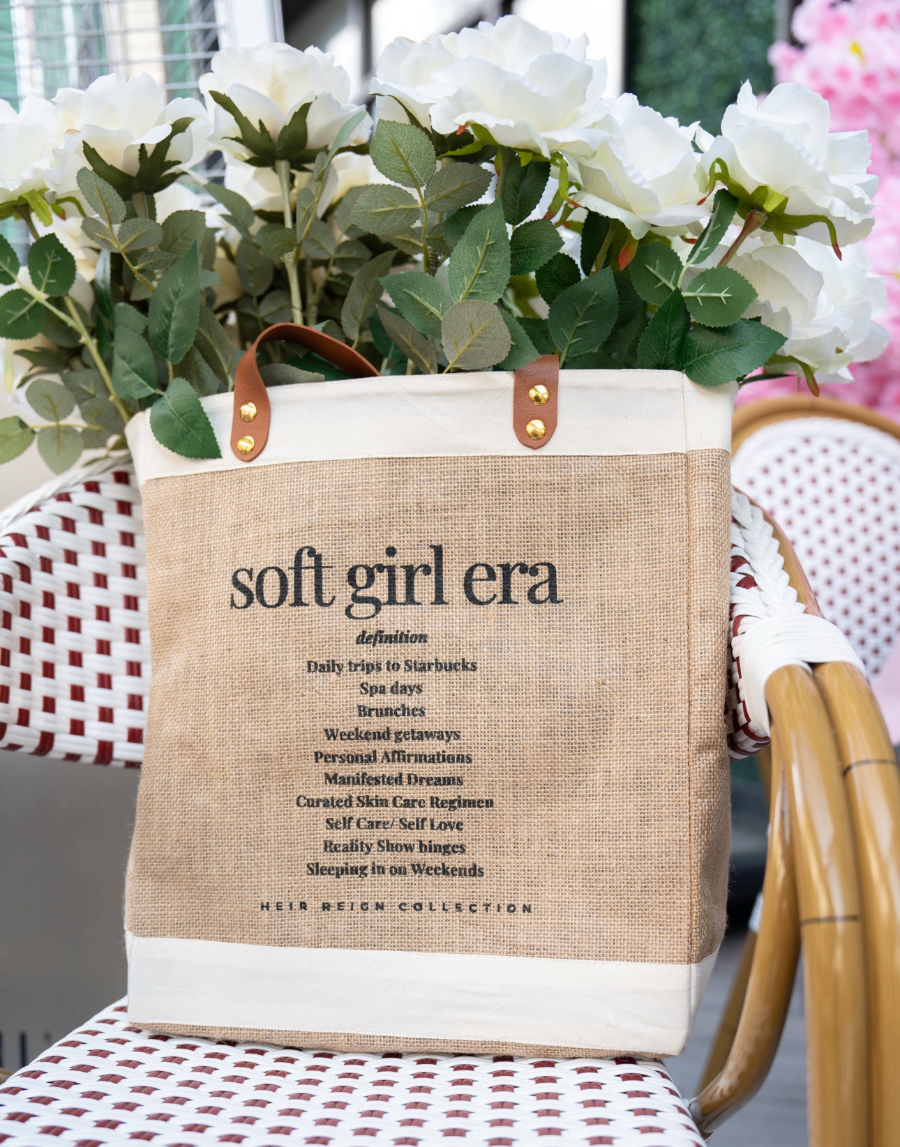This is a picture of a burlap tote bag with a positive affirmation quote on the front. There is a woman holding the tote bag that has bright white summer flowers inside of the bag.