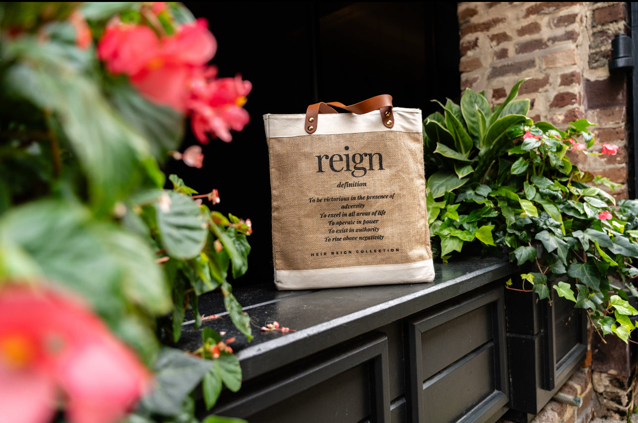 This is a picture of a burlap tote bag with a positive affirmation quote on the front. It is in a beautiful outdoor setting.