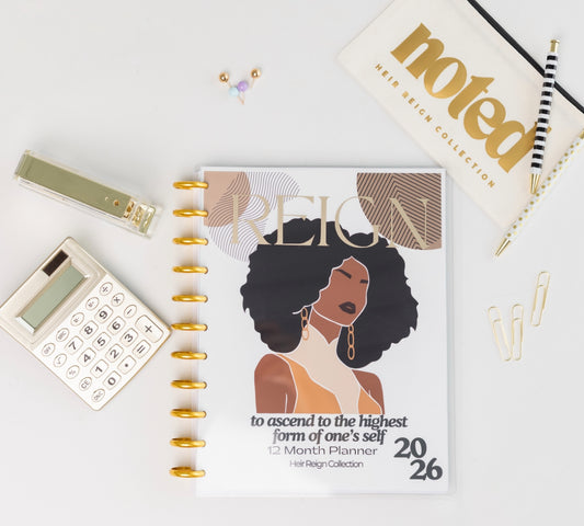 Planner with a woman's illustration on the cover, placed on a white surface with stationery items. Reign Empowerment 12-Month Planner featuring Black woman illustration in gold, Luxury refillable disc-bound planner USA with empowerment cover
