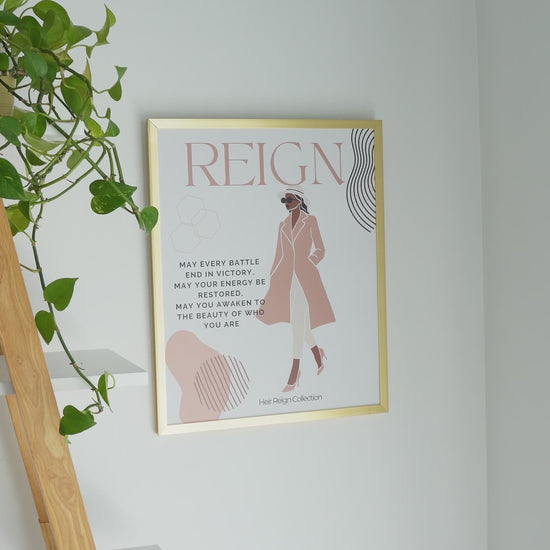 Beautiful wall art illustration of a black woman. She is wearing a pink trench coat, white  pants and high heel shoes. The picture also has an inspirational positive affirmation next to the woman. The picture is in a  gold frame with beautiful home decor. 