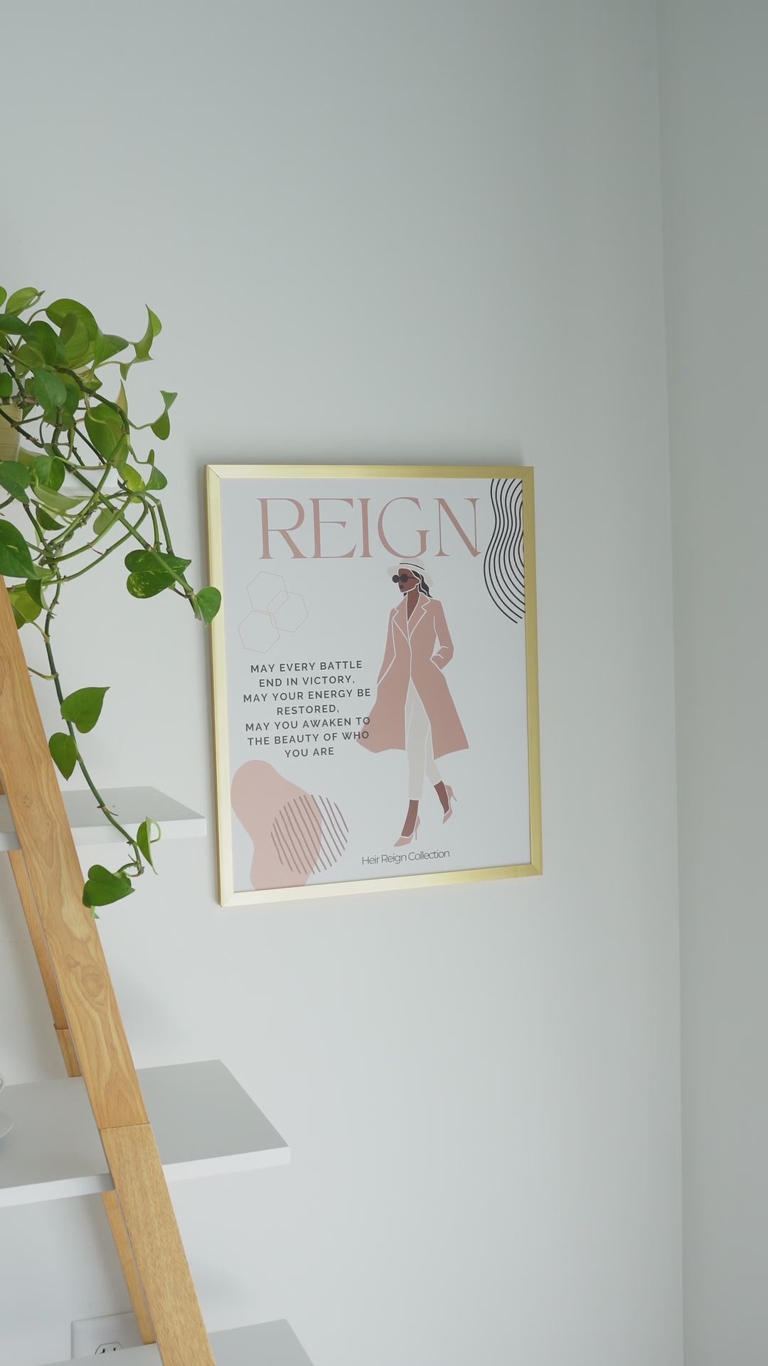 Beautiful wall art illustration of a black woman. She is wearing a pink trench coat, white  pants and high heel shoes. The picture also has an inspirational positive affirmation next to the woman. The picture is in a  gold frame with beautiful home decor. 